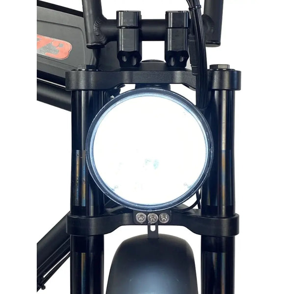 Close-up of the Cruz73 Unlimited Retro Fat Tyre 750W electric bike round LED headlight illuminated.