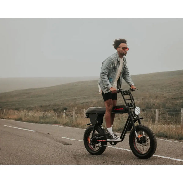 Rider standing while cruising on the Cruz73 Unlimited Retro Fat Tyre Electric Bike 750W along a rural road.