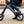 Close-up view of the Cruzaa E-Scooter Pro in black being ridden on a gravel surface, highlighting the sturdy frame and footrests.
