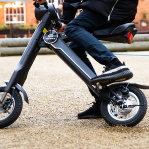 Close-up view of the Cruzaa E-Scooter Pro in black being ridden on a gravel surface, highlighting the sturdy frame and footrests.