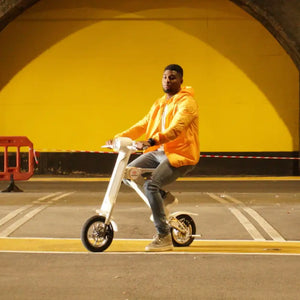 Side profile of a man in a yellow jacket riding the white Cruzaa E-Scooter Pro, demonstrating the seated riding position and compact wheelbase.