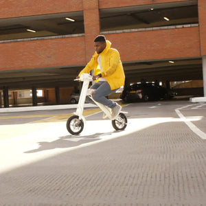 A man in a yellow jacket riding the white Cruzaa E-Scooter Pro through a covered parking area, highlighting the scooter's agility.