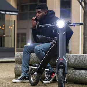 A commuter sitting on the black Cruzaa E-Scooter Pro while checking his phone, showcasing the scooter's comfortable seated design.