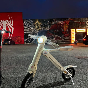 The white Cruzaa E-Scooter Pro parked at night in front of colourful street art, emphasizing its modern aesthetic and built-in lighting.