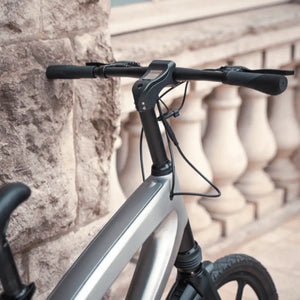 Close-up detail of the Cruzaa electric bike's sleek handlebar stem and integrated digital display, captured against a textured stone wall background.