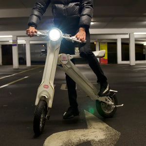 A man in a black puffer jacket riding the white Cruzaa E-Scooter Pro along a cobbled canal path, showcasing its versatility on different urban surfaces.