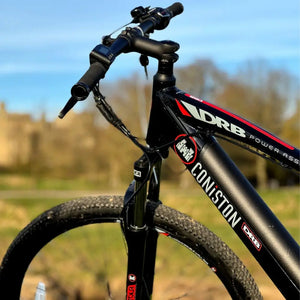 Close-up of the front end of the Dallingridge Coniston e-bike showing the headtube logo, suspension fork, and castle background.