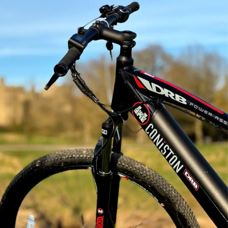 Close-up of the front end of the Dallingridge Coniston e-bike showing the headtube logo, suspension fork, and castle background.