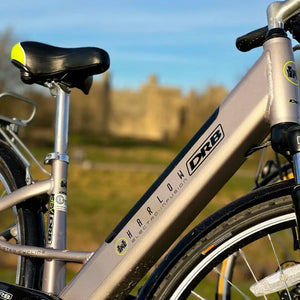Side view of the silver Dallingridge Harlow frame showing the top tube, integrated battery downtube, and model logo with a castle in the background.