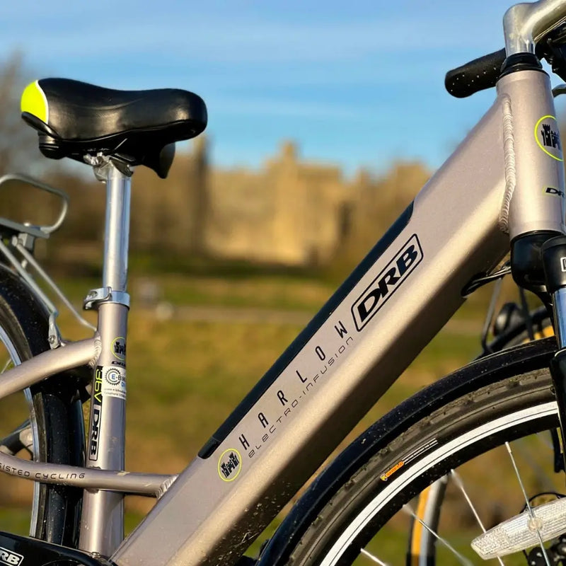 Side view of the silver Dallingridge Harlow frame showing the top tube, integrated battery downtube, and model logo with a castle in the background.