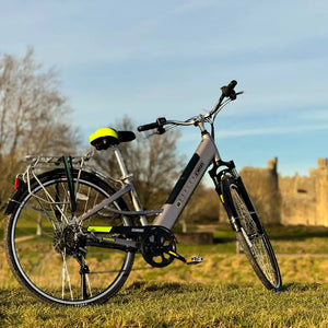 Rear-angled view of the silver Dallingridge Harlow hybrid electric bike parked on a grassy hill, highlighting the rear rack, mudguards, and step-through frame design.