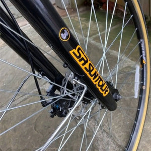Close-up detail of the front wheel showing the black SR Suntour suspension fork, mechanical disc brake caliper, and spokes on the Dallingridge Malvern.