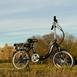 Dallingridge Oxford electric folding bike parked on a grassy hill with a historic castle in the background, showcasing its step-through frame.