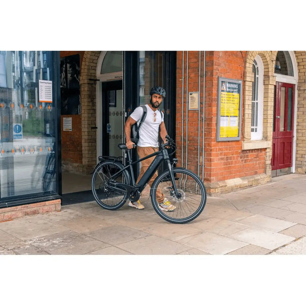 Man standing outside a building holding the Dawes Spire 1.0 Crossbar electric hybrid bike, wearing a helmet and backpack.