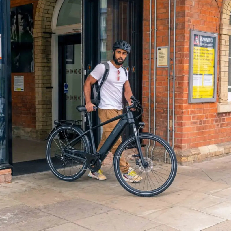 Man standing outside a building holding the Dawes Spire 1.0 Crossbar electric hybrid bike, wearing a helmet and backpack.