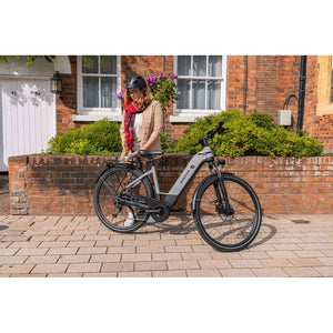 A woman standing next to a Dawes Spire 2.0 Cues Low Step electric hybrid bike 250W in a residential street, wearing a helmet.