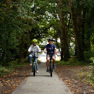 Two riders on E-Go folding e-bikes on a woodland path, one on a Duck Egg CarbonStep