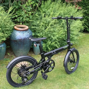 Side profile of the E-Go Lite+ folding electric bike in satin black parked in a garden, showcasing its compact frame, 20-inch wheels, and 7-speed derailleur system.