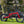 Gloss red E-Go Max+ folding electric bike parked on a sunny lawn, highlighting its robust aluminium frame and 20-inch alloy wheels suitable for outdoor leisure.
