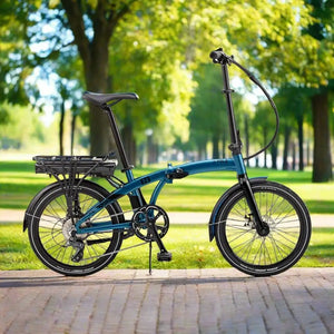 Metallic blue EZEGO Fold electric folding bike standing on a paved path in a park with sunlit trees in the background.