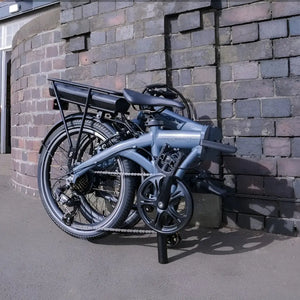 Falcon Compact electric folding bike 250W folded and parked outdoors against a brick wall, highlighting compact storage for city use.