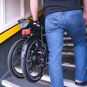 Falcon Compact electric folding bike 250W being carried upstairs in folded position, demonstrating portability and compact design.