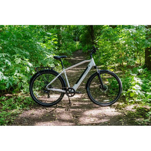 Falcon Horizon Crossbar electric hybrid bike in silver parked on a forest trail, surrounded by lush green foliage.