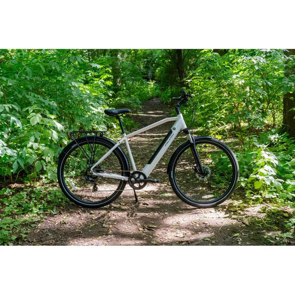 Falcon Horizon Crossbar electric hybrid bike in silver parked on a forest trail, surrounded by lush green foliage.
