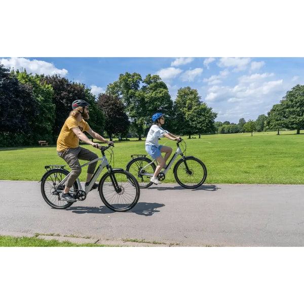 Two cyclists riding Falcon Horizon electric hybrid bikes in a park on a sunny day.