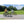Two cyclists riding Falcon Horizon Low Step electric hybrid bikes in a park on a sunny day.