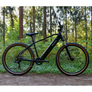 Side profile of the black Falcon Turbine 250W electric mountain bike parked on a woodland trail, showcasing its rugged frame and tan wall tires in an off-road setting.