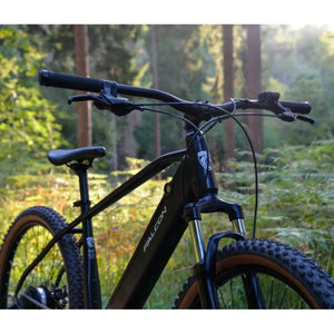 Front-facing view of the Falcon Turbine electric mountain bike in a woodland setting, focusing on the front suspension fork absorbing terrain and the wide riser handlebars.
