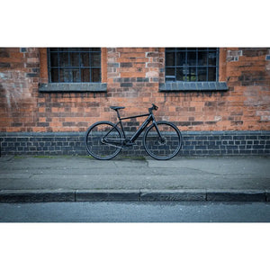 Falcon Zone Single Speed electric hybrid bike parked outdoors against a brick wall, showcasing its sleek and modern design.