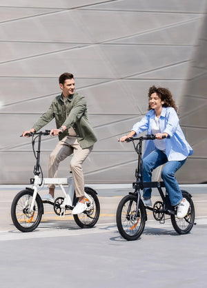 Two riders pedalling folding electric bikes down a road.