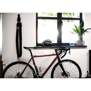 Hiplok Home Gold chain lock neatly hanging on a wall hook in a modern indoor setting next to a red road bike.