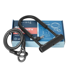 Hygge D-Lock with keys and double loop cable placed on top of the retail packaging for secure bike locking.