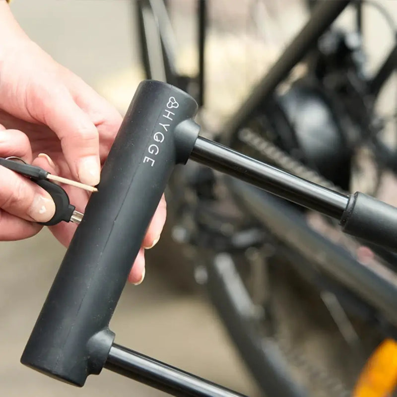 Close-up view of hands using a key to unlock a matte black Hygge D-lock on an electric bicycle.