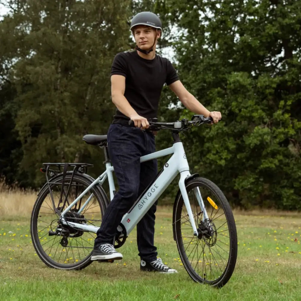 Rider using the Hygge Lossø Commuter Hybrid Electric Bike 250W on a grassy field with trees in the background.