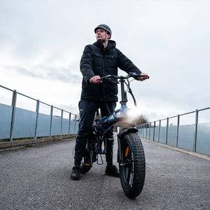 A rider in a winter jacket standing with his Hygge Sorø 2025 electric bike on a bridge during an overcast commute.