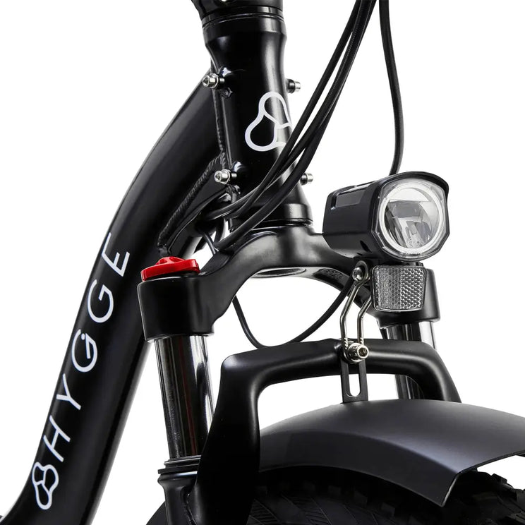 Close-up of the bright LED headlight and front suspension fork on the black Hygge Vester Step electric bike.
