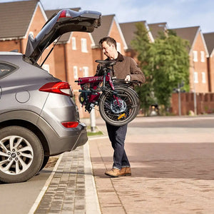 A man loading a folded Hygge Virum electric bike into a car trunk, highlighting its compact size for travel and storage.