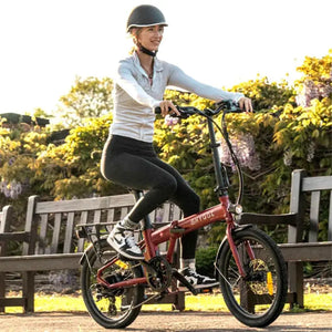 Rider cycling the Hygge Virum Folding Electric Bike on a paved path in a green outdoor setting.