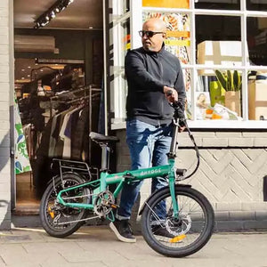 Adult commuter walking with the Hygge Virum Folding Electric Bike in an urban shopping street setting.