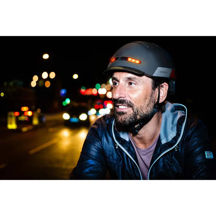 Man wearing the Livall BH51M Neo smart helmet during night cycling, with bright LED lights and city traffic in the background.