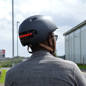 Rear view of a cyclist wearing a blue Livall C20 smart helmet with rear LED lights, riding along an urban street.