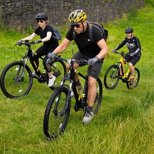 A group of cyclists riding Mark2 Scrambler electric mountain bikes up a grassy hill, showcasing the powerful motor's ability to tackle inclines with ease.