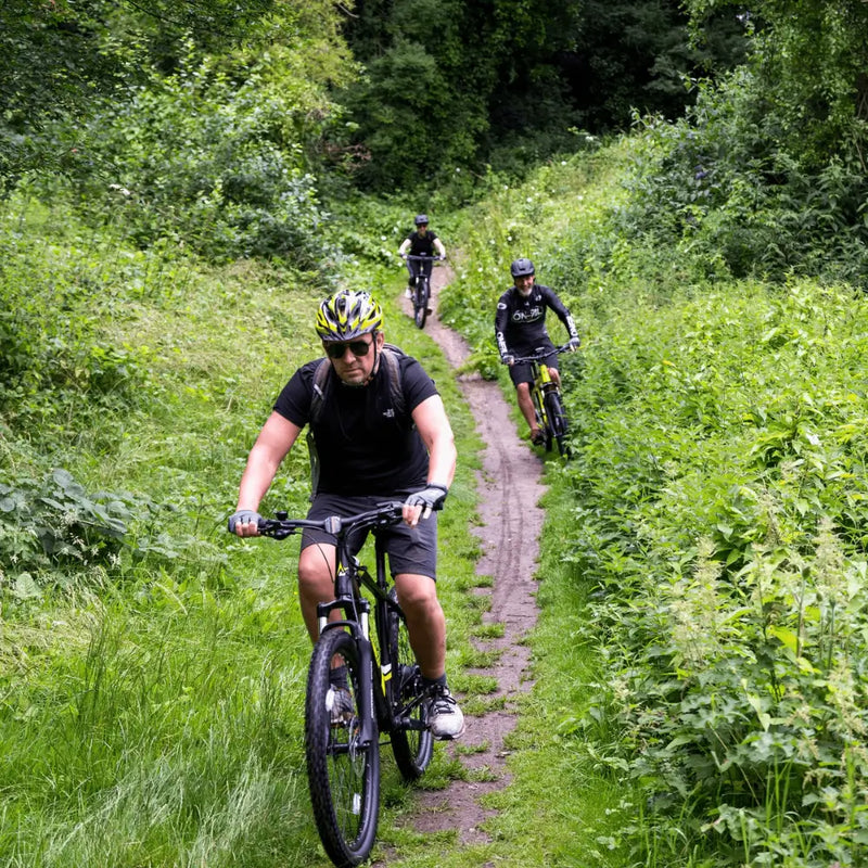 A rider navigating a narrow forest path on the Mark2 Scrambler hardtail e-bike, demonstrating its agility and suspension on off-road terrain.