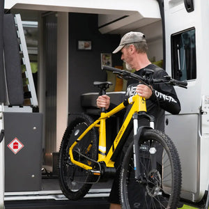 A man lifting the lightweight yellow Mark2 Scrambler electric bike into a camper van, highlighting its portability for adventure travel.