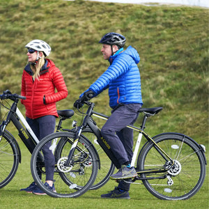 A couple in winter jackets standing next to their Mark2 X-Cross 520 e-bikes on a grassy hill.
