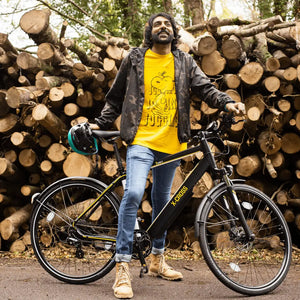 Man standing next to his black Mark2 X-Cross 520 hybrid e-bike near a stack of logs in a forest.
